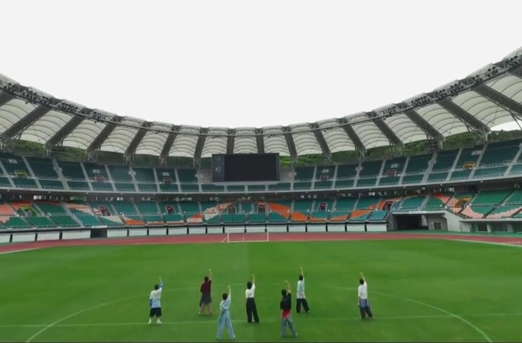 エコパスタジアムのピッチ中央に集まるTravis Japanメンバー7人全員とスタジアム全景